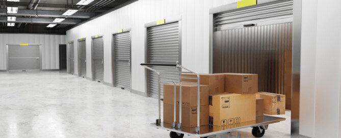 A silver rolling cart stacked with cardboard boxes sits in the doorway of a partially open storage unit.