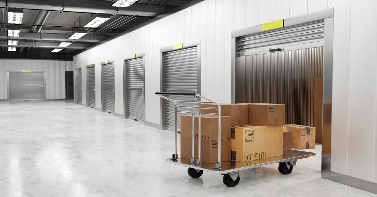 A silver rolling cart stacked with cardboard boxes sits in the doorway of a partially open storage unit.