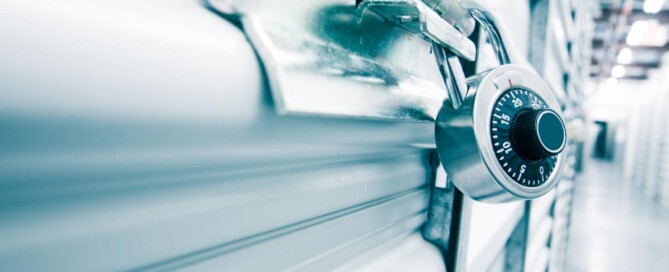 A close-up of a silver combination lock securing a storage unit door, with a blurred hallway in the background.