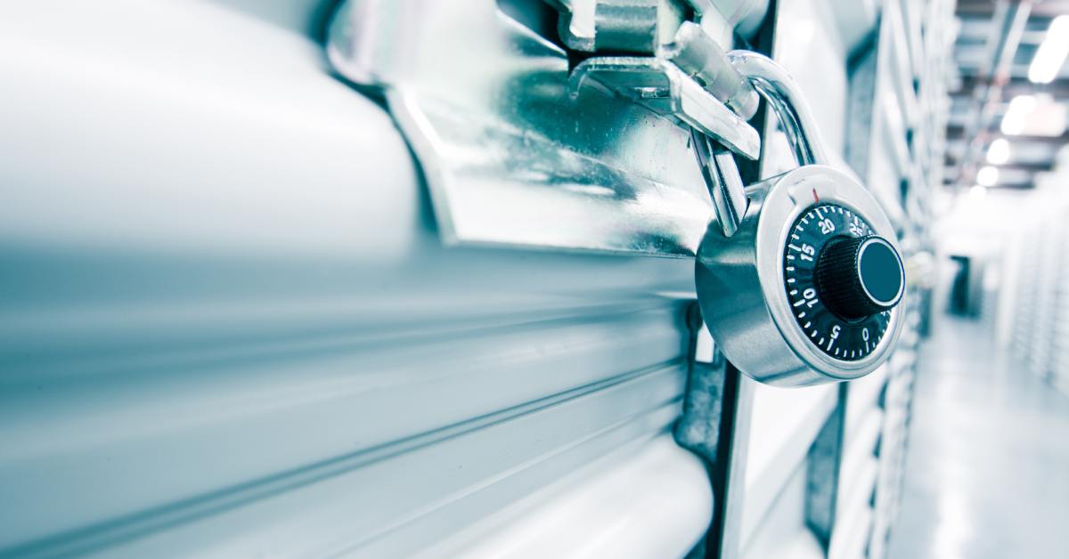 A close-up of a silver combination lock securing a storage unit door, with a blurred hallway in the background.