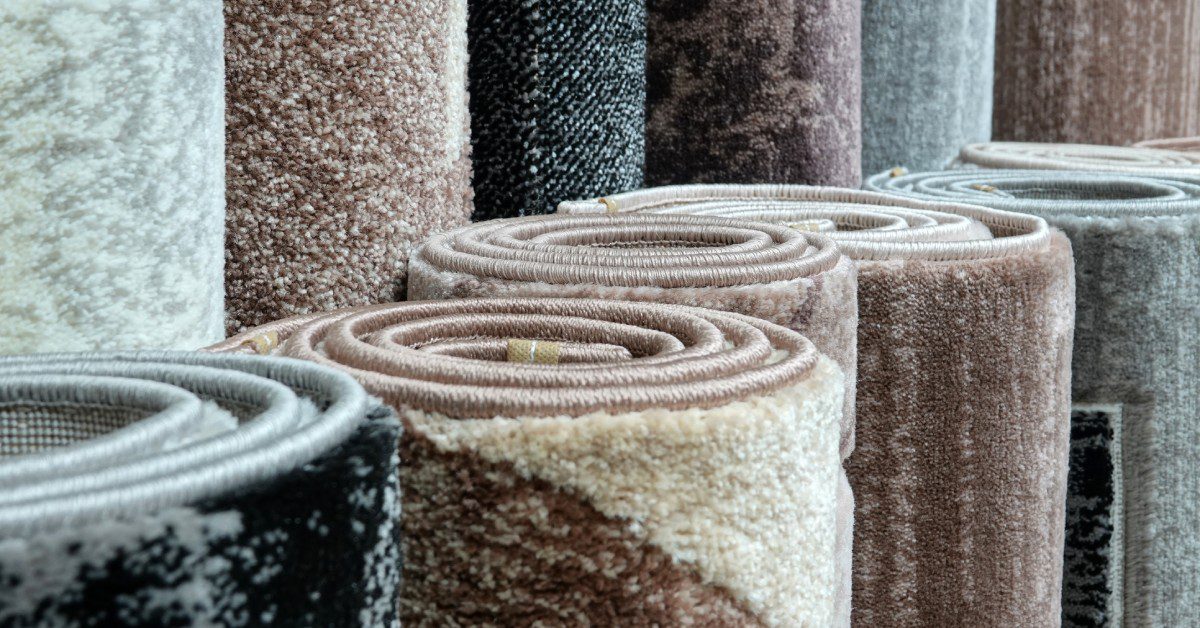 A close-up of rolled carpets in neutral tones like beige, gray, and black, showcasing varied textures and patterns.