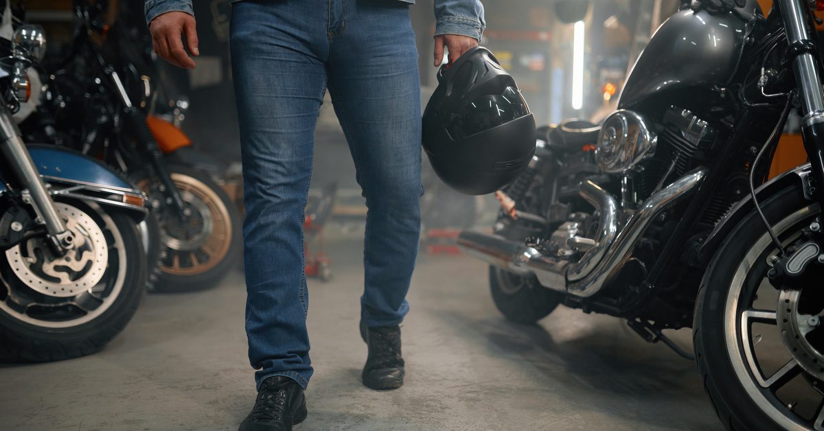 A man wearing jeans and holding a helmet walks through his garage while several large motorcycles sit nearby.