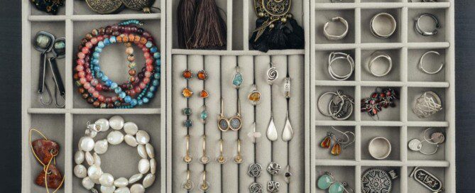 An open jewelry organizer displays bracelets, rings, earrings, and necklaces neatly arranged in soft-lined compartments.