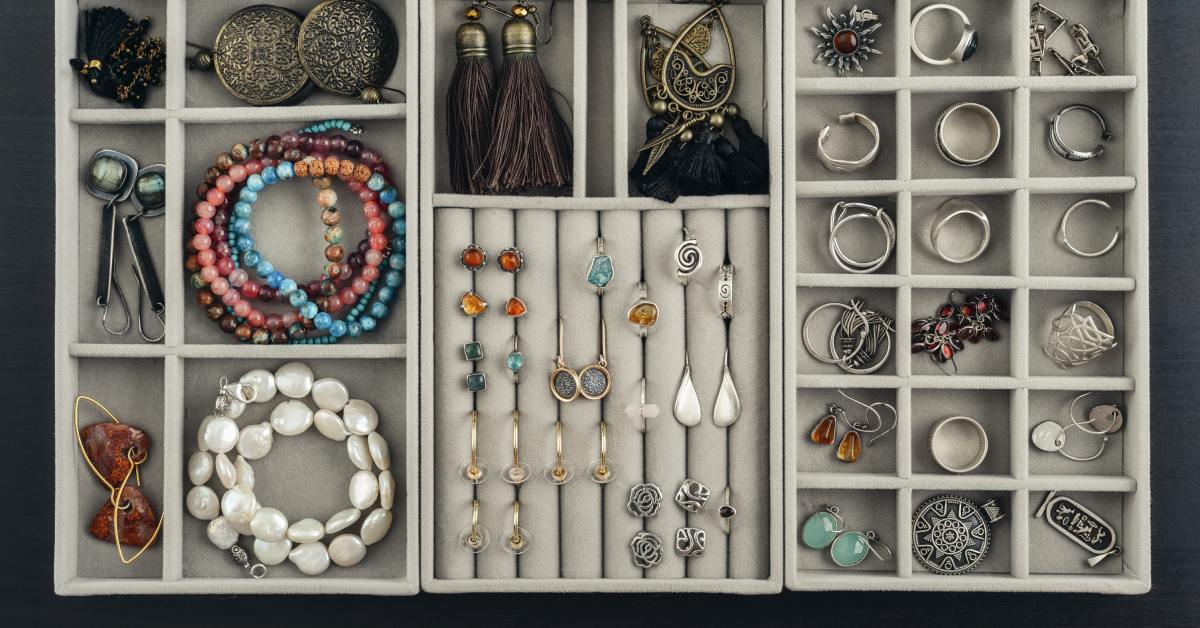 An open jewelry organizer displays bracelets, rings, earrings, and necklaces neatly arranged in soft-lined compartments.