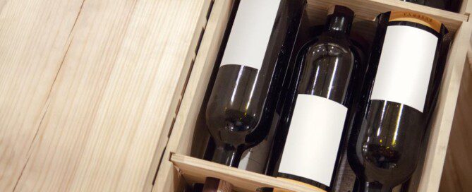 A wooden crate holds several wine bottles on their sides, each secured in divided compartments with labels facing outward