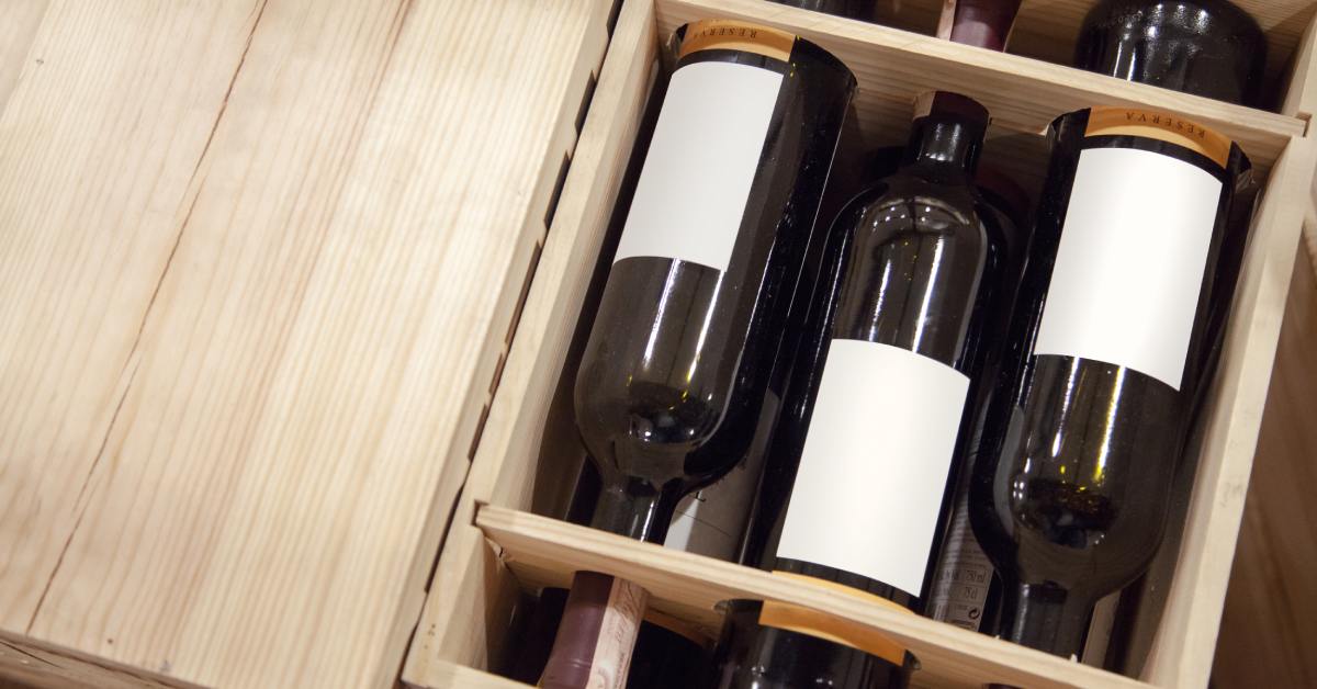 A wooden crate holds several wine bottles on their sides, each secured in divided compartments with labels facing outward