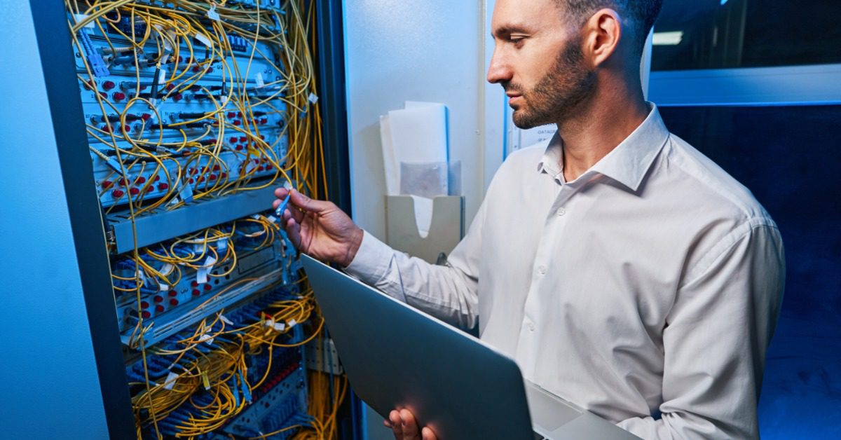 A technician holds server drives beside an open rack while rows of data center equipment glow in the background.